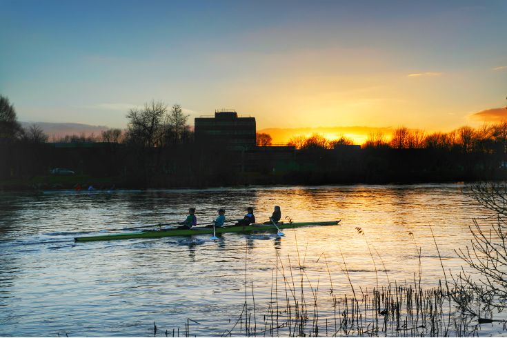 four people rowing in the river at sunset